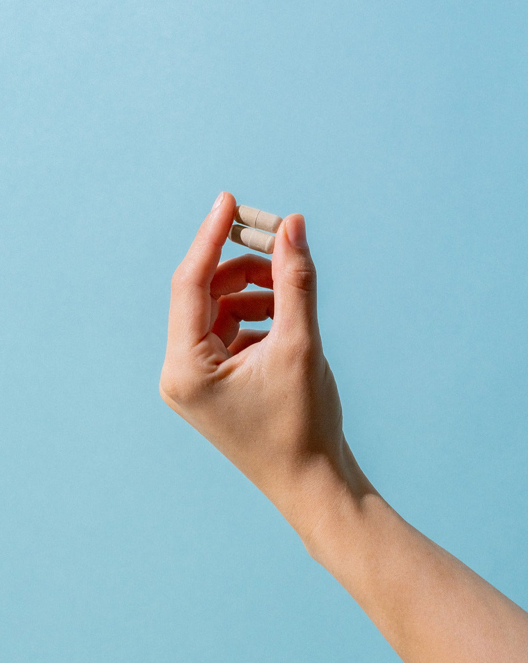 The Baseline pills being held up by two fingers in front of a blue background