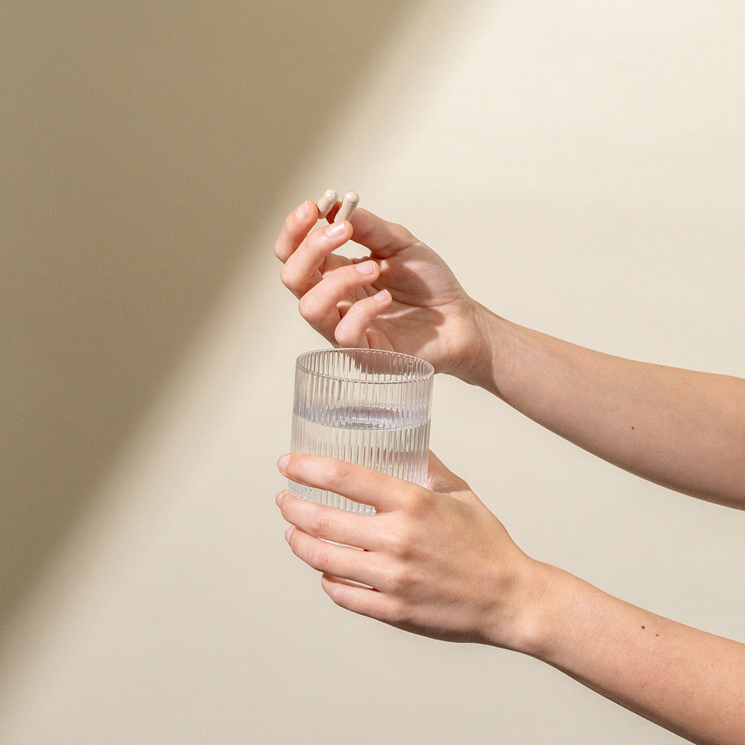 Hand holding a glass of water and two pills
