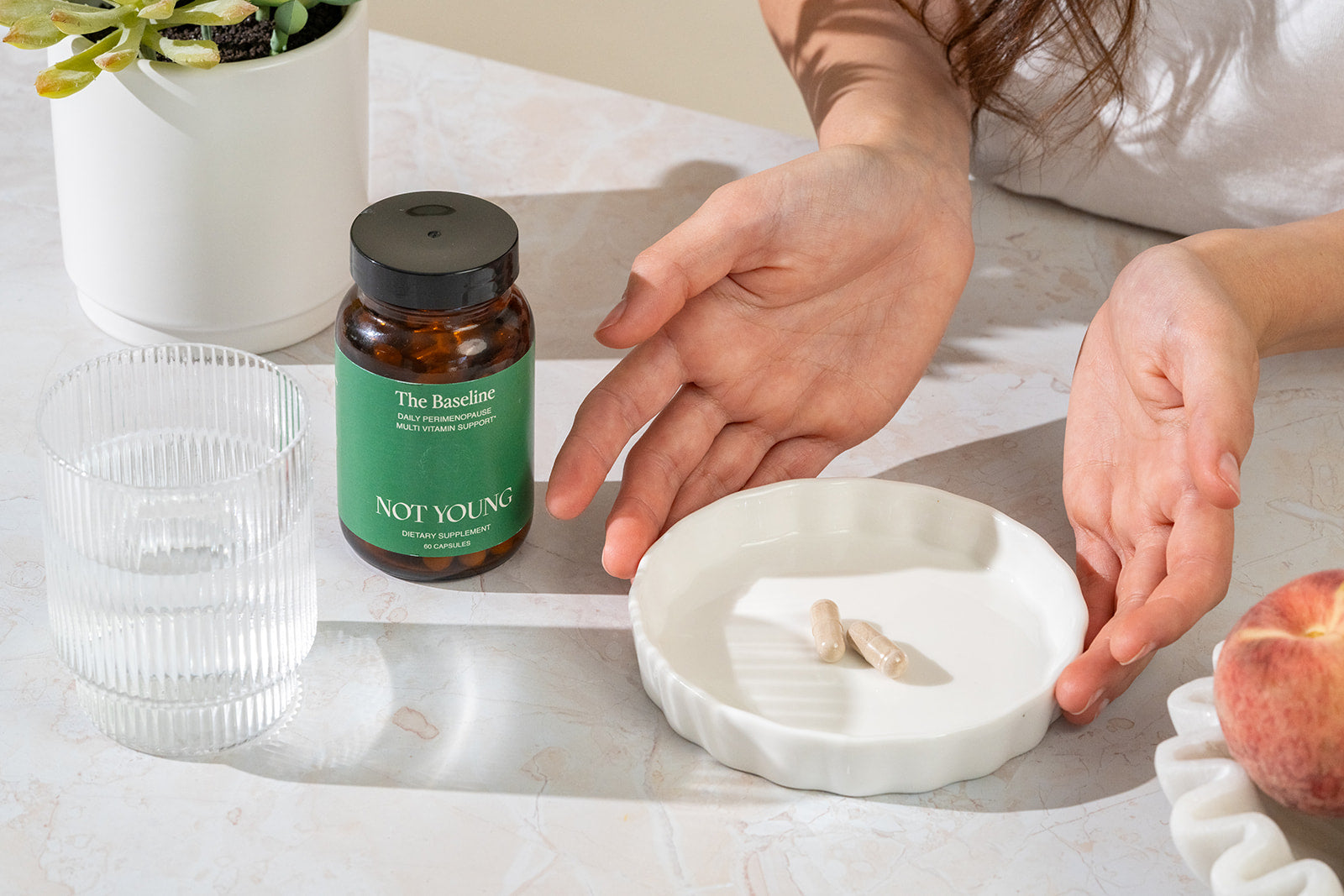 Two pills on a ceramic tray with The Baseline and a glass of water next to it